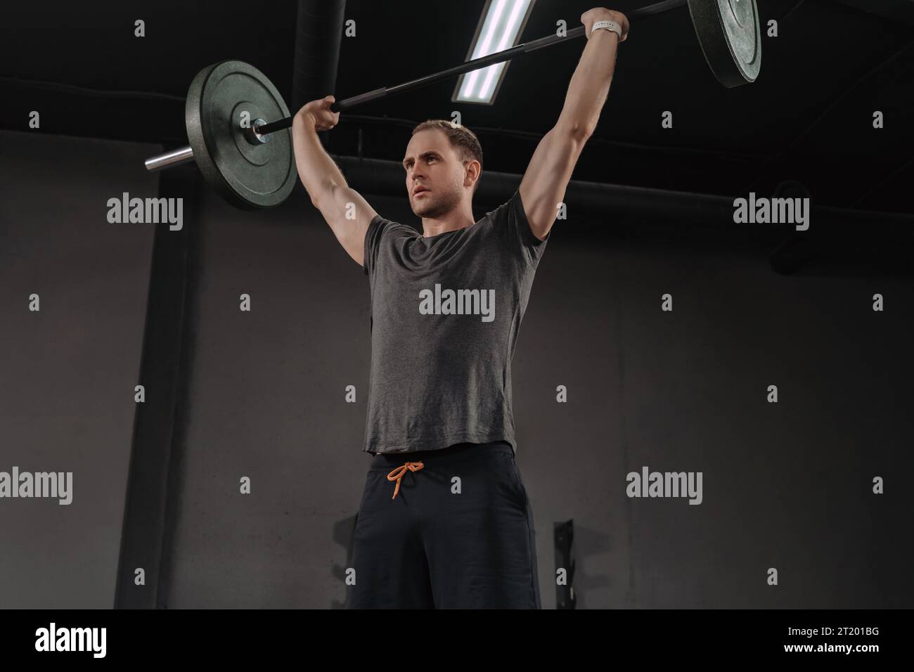 Starker muskulöser Mann, der schwere Langhantel über dem Crossfit-Fitnessstudio hält und militärische Pressetraining als Teil des funktionellen Trainings macht. Gewichtheber mit Langhantel trainieren. Stockfoto