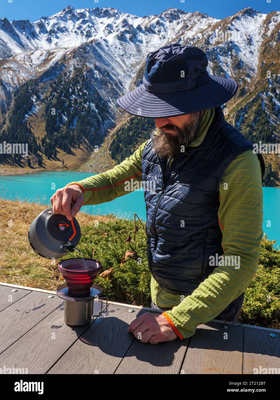 Bärtiger männlicher Tourist, der Kaffee zubereitete, während er hoch in den Bergen zelte. Wandern im Hochland. Frühstück während der Reise zubereiten Stockfoto
