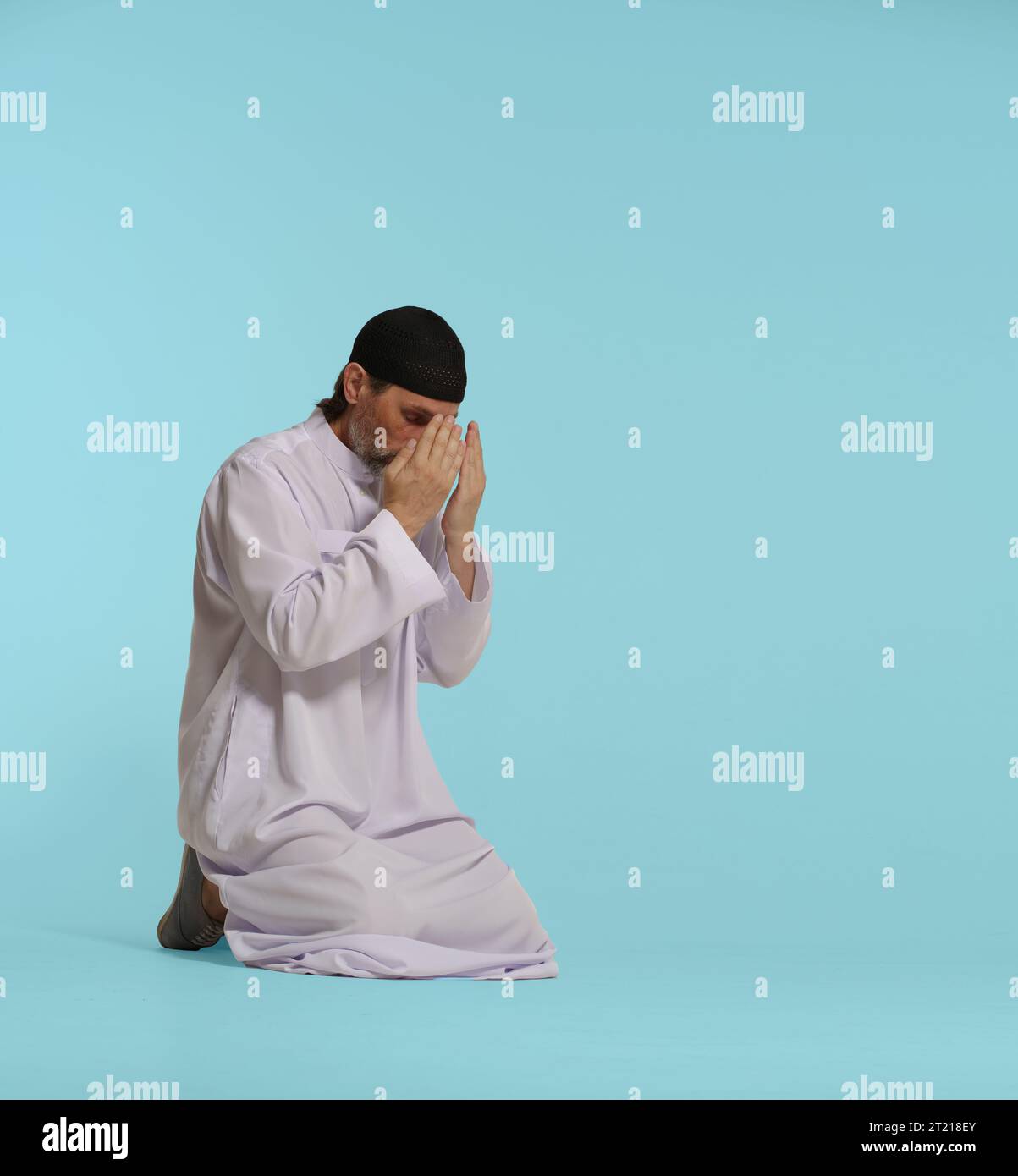 Ein frommer muslimischer Mann kniet im Gebet, Hände bedecken das Gesicht im Akt des Namaz, ein grundlegendes islamisches Ritual. Isoliert auf blauem Hintergrund. Glaube, Spiritualität und Hingabe in der Praxis des islamischen Gebets. Hochwertige Fotos Stockfoto
