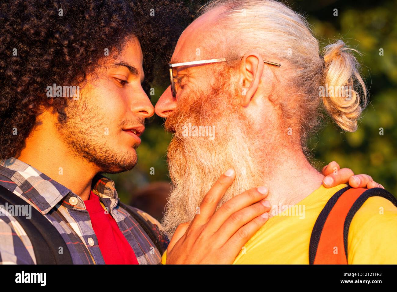 Ein zärtlicher und leidenschaftlicher Moment, der als attraktiver schwuler Arabianer mit langen lockigen Haaren und sein älterer männlicher Liebhaber mit langen grauen Haaren und einem Bart sich anstarren, der in der warmen Umarmung der untergehenden Sonne einen leidenschaftlichen Kuss teilt. Intimer Sonnenuntergang-Moment, Kuss des Schwulen-Paares. Hochwertige Fotos Stockfoto