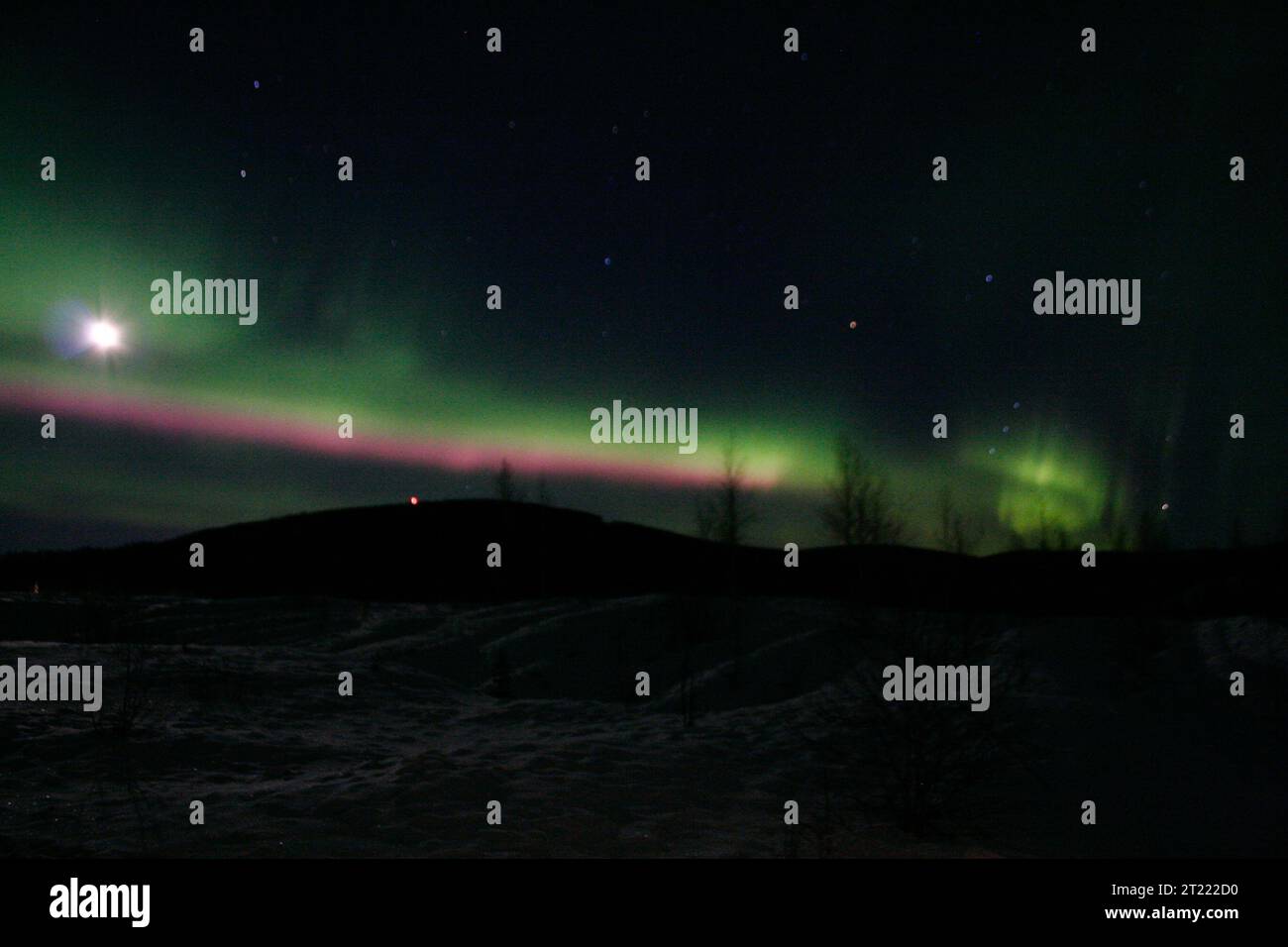 Die aurora Borealis verläuft über den Horizont Alaskas, ihre wechselnden Lichter in Grün- und Rottönen beleuchten die Nacht über der Tundra. Stockfoto