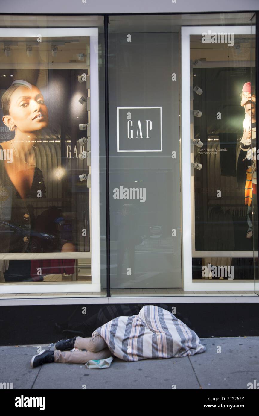 Obdachloser Mann schläft auf dem Gehweg vor einem GAP Store im Times Square Viertel von Manhattan, NYC. Stockfoto