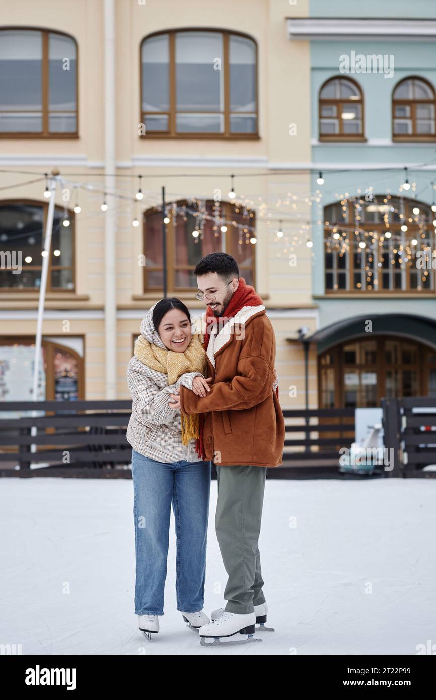 Vertikales Porträt in voller Länge eines jungen Paares, das gemeinsam auf einer Eislaufbahn im Freien läuft und im Winter Spaß hat Stockfoto