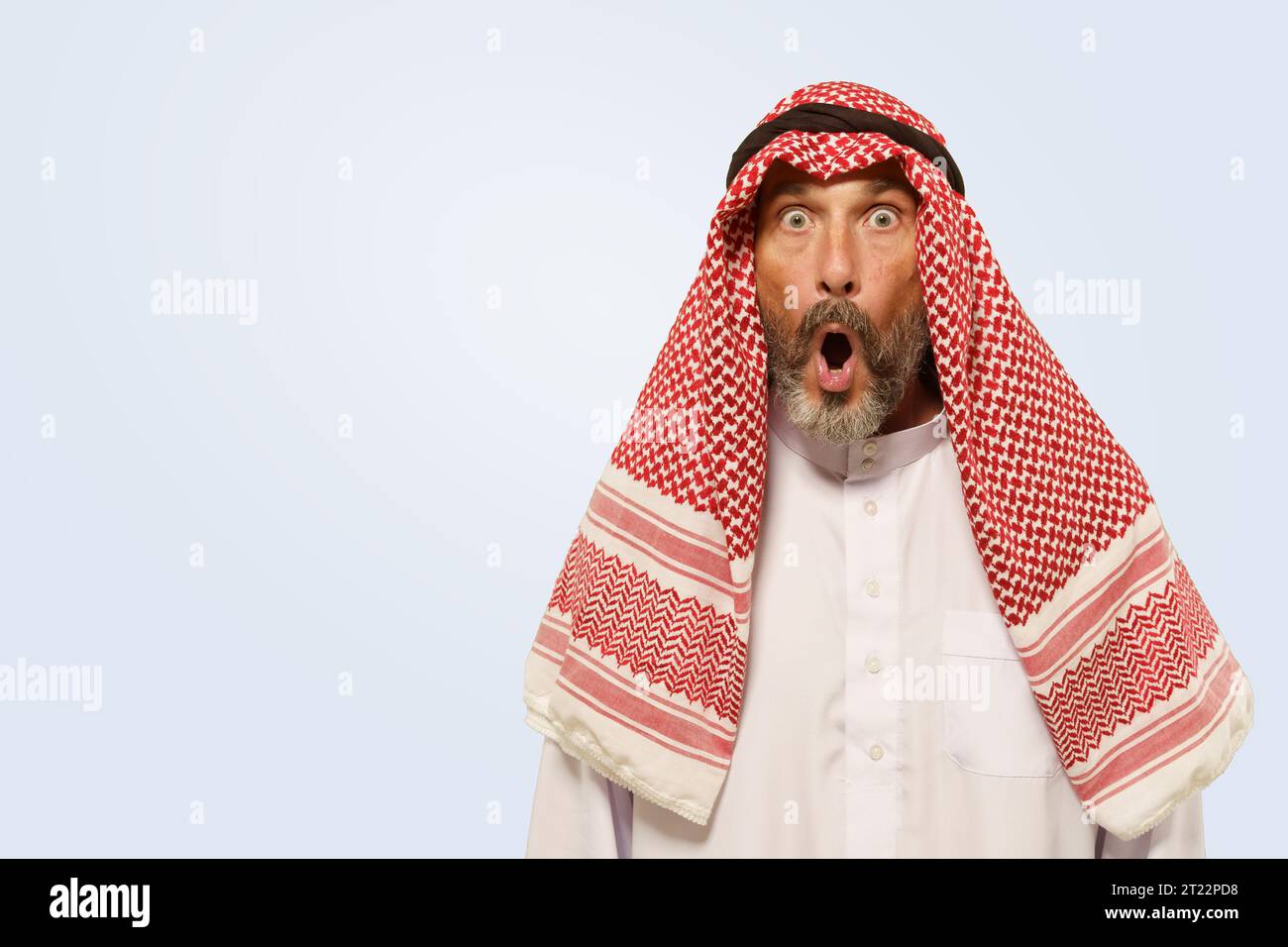 Der arabische Mann zeigt in keffiyeh einen Ausdruck mit Schock, Überraschung und Frustration, der sich durch den geöffneten Mund widerspiegelt. Er isolierte auf sanftem hellblauem Hintergrund und veranschaulichte die kulturelle Identität der ethnischen Gruppe. Hochwertige Fotos Stockfoto