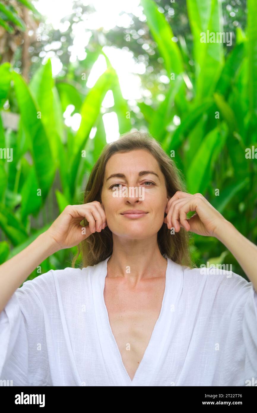 Vertikales Porträt einer Frau mittleren Alters bei einer Gesichts- und Nackenmassage. Selbstgesichtsmassage und tägliche Hautpflege im Erwachsenenalter. Bio-Kosmetik für Stockfoto