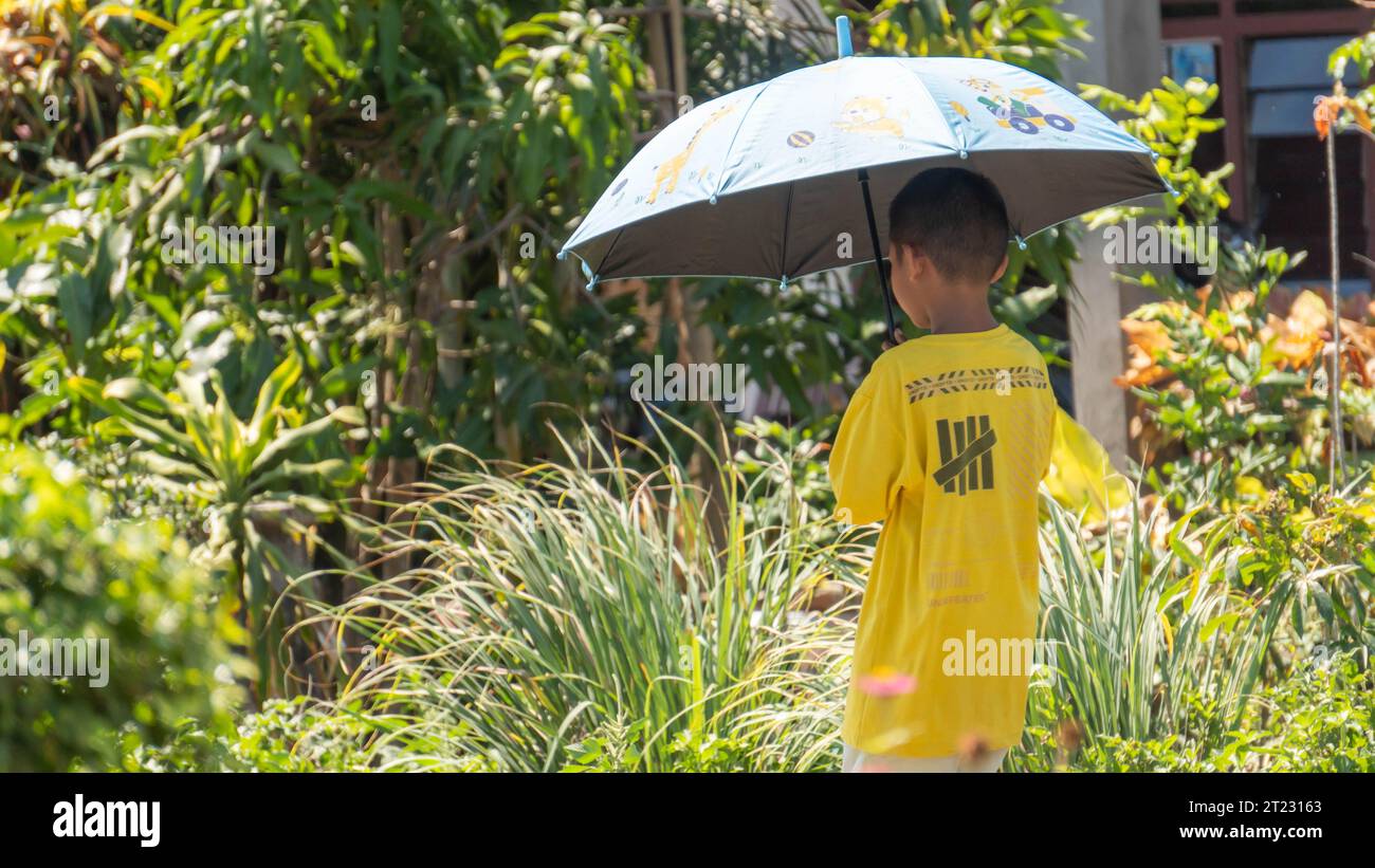 Pinrang Indonesia, 16. Oktober 2023: Ein Junge läuft mit einem Sonnenschirm unter der sengenden heißen Sonne. Nachmittag im Dorf Masolo Pinrang, Indonesien Stockfoto