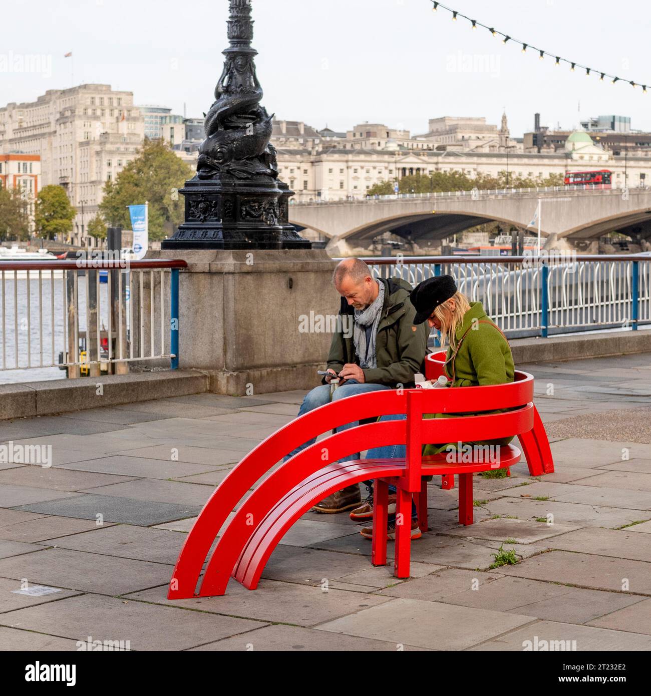 Menschen, die im Freien Mobiltelefone benutzen, auf einer roten Bank sitzen, London, Großbritannien Stockfoto