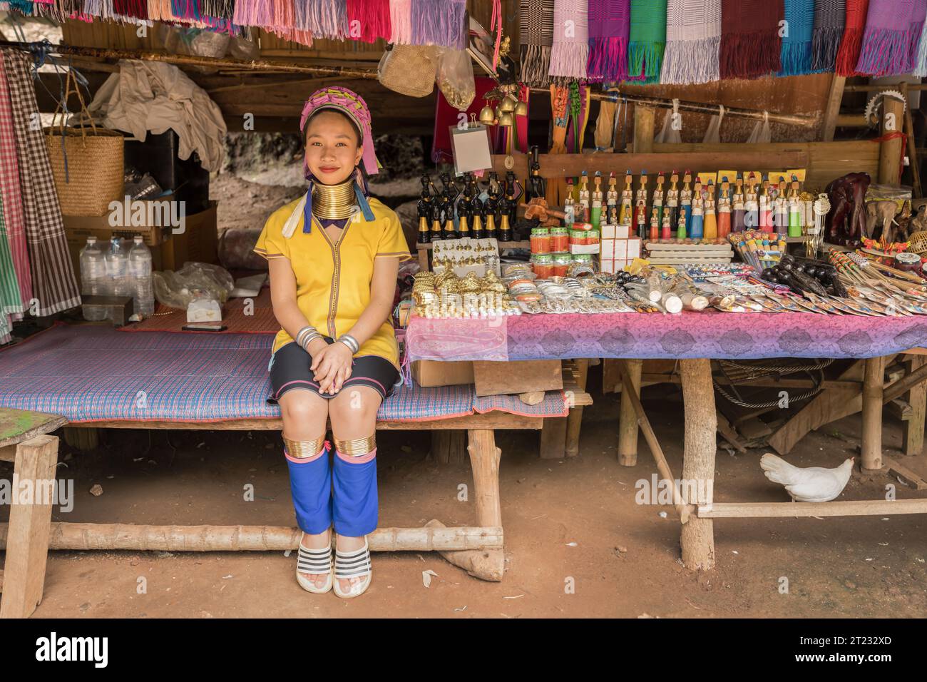 Karen Frau aus Pai in Mae Hong Son, Thailand, mit Messing Halsringen sitzt auf einer Holzschaukel im rustikalen Dorf und trägt ein farbenprächtiges Karen Kleid Stockfoto