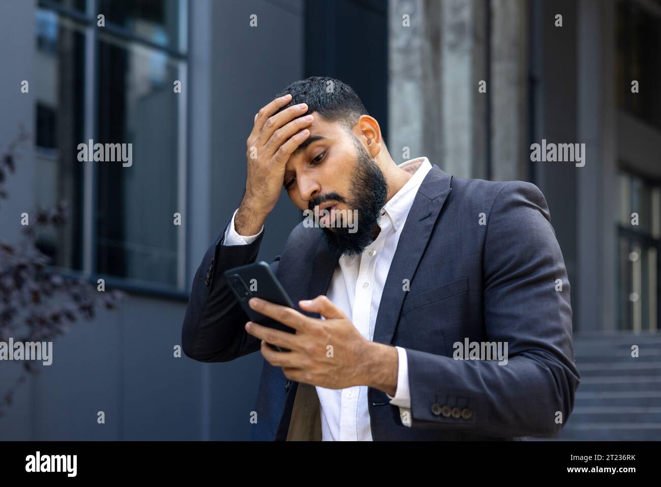 Verärgerter muslimischer Geschäftsmann, der in der Nähe des Büros stand und Kopf hielt, schockiert Nachrichten liest, Nachricht empfangen. Stockfoto