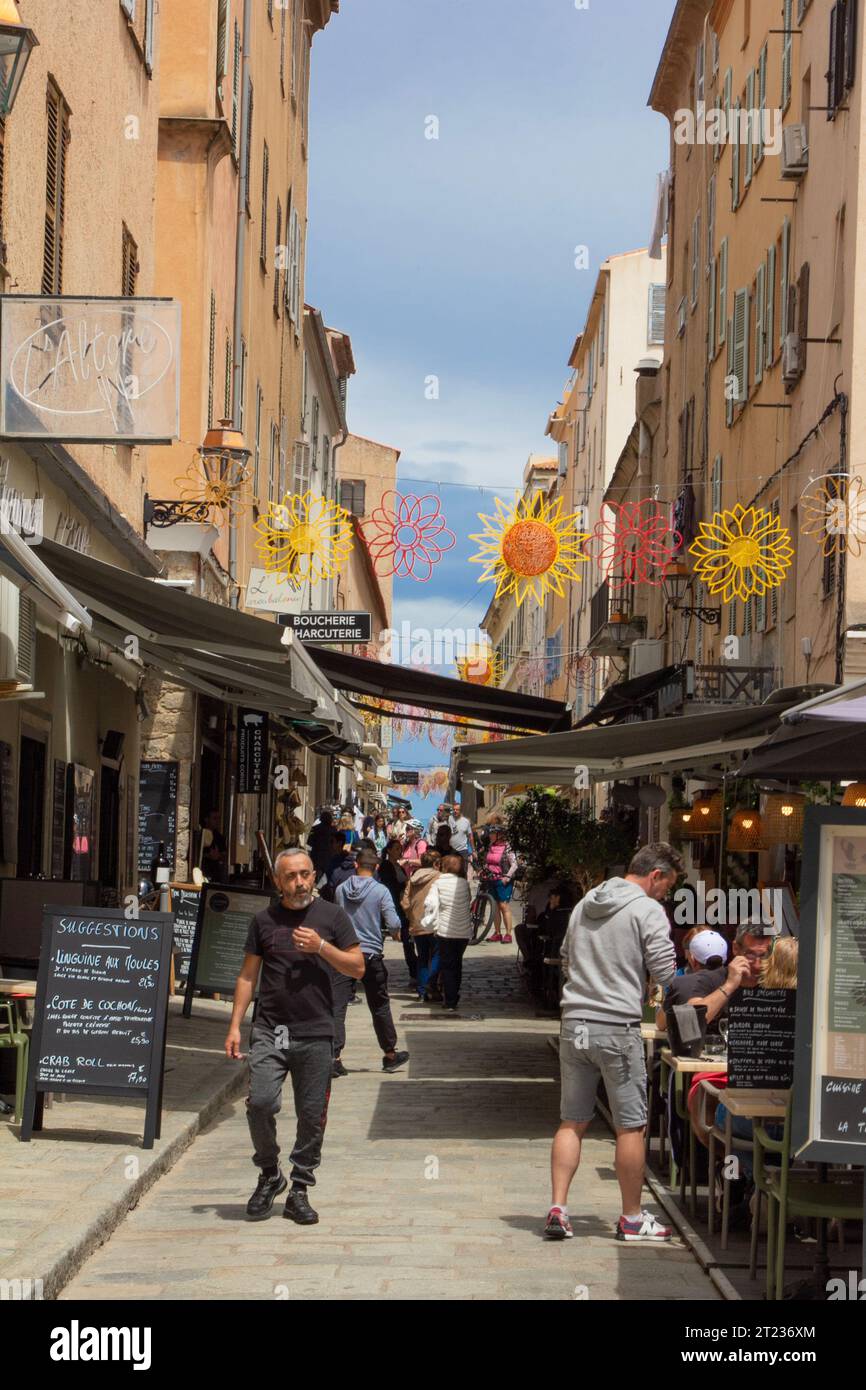 Frankreich, Korsika, l'Ile-Rousse, Rue Dominique Fioravanti: Einkaufslustige füllen die fröhlich geschmückte Gasse im Schatten der Markisen. Stockfoto