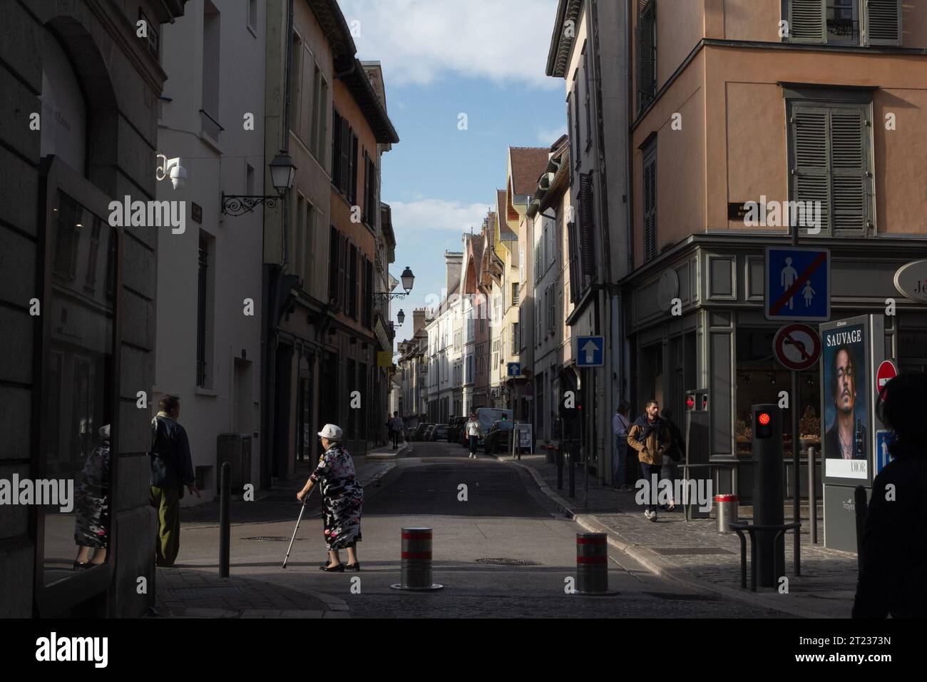 Eine ältere, gehütete Dame mit Krücken überquert die Straße in Troyes, Frankreich, und ihr Bild spiegelt sich in einem Schaufenster wider. Stockfoto