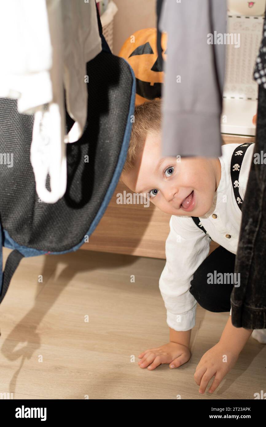 Halloween-Konzept. Ein kleiner gutaussehender Junge versteckt sich und macht Gesichter vor dem Hintergrund eines orangen Kürbis. Nahaufnahme Stockfoto