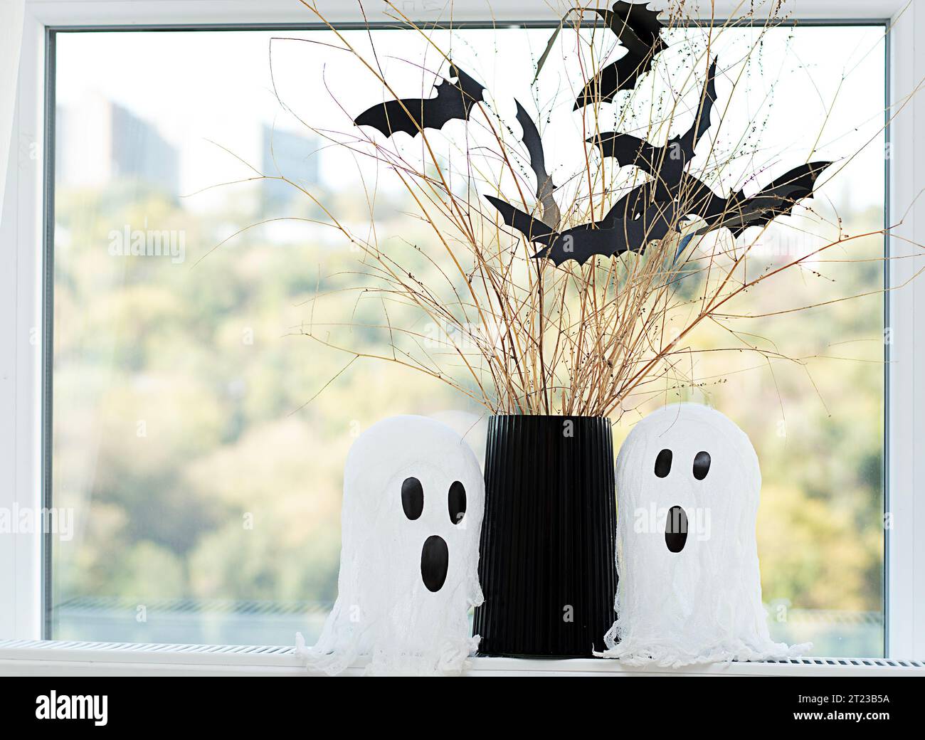 Halloween. Konzept. Herbstferien. Layout. Hintergrund. Zwei weiße Geister und eine schwarze Vase mit trockenen Zweigen und Fledermäusen aus Papier gegen den Hinterkopf Stockfoto