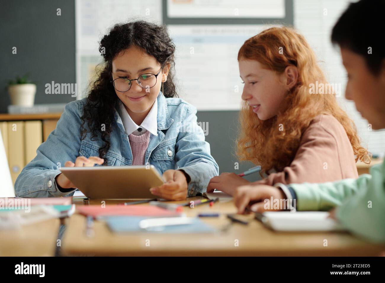Zwei niedliche interkulturelle Schülerinnen bereiten die Präsentation englischer Wörter oder neuer Grammatikregeln vor, während eines von ihnen den Gadget-Bildschirm berührt Stockfoto