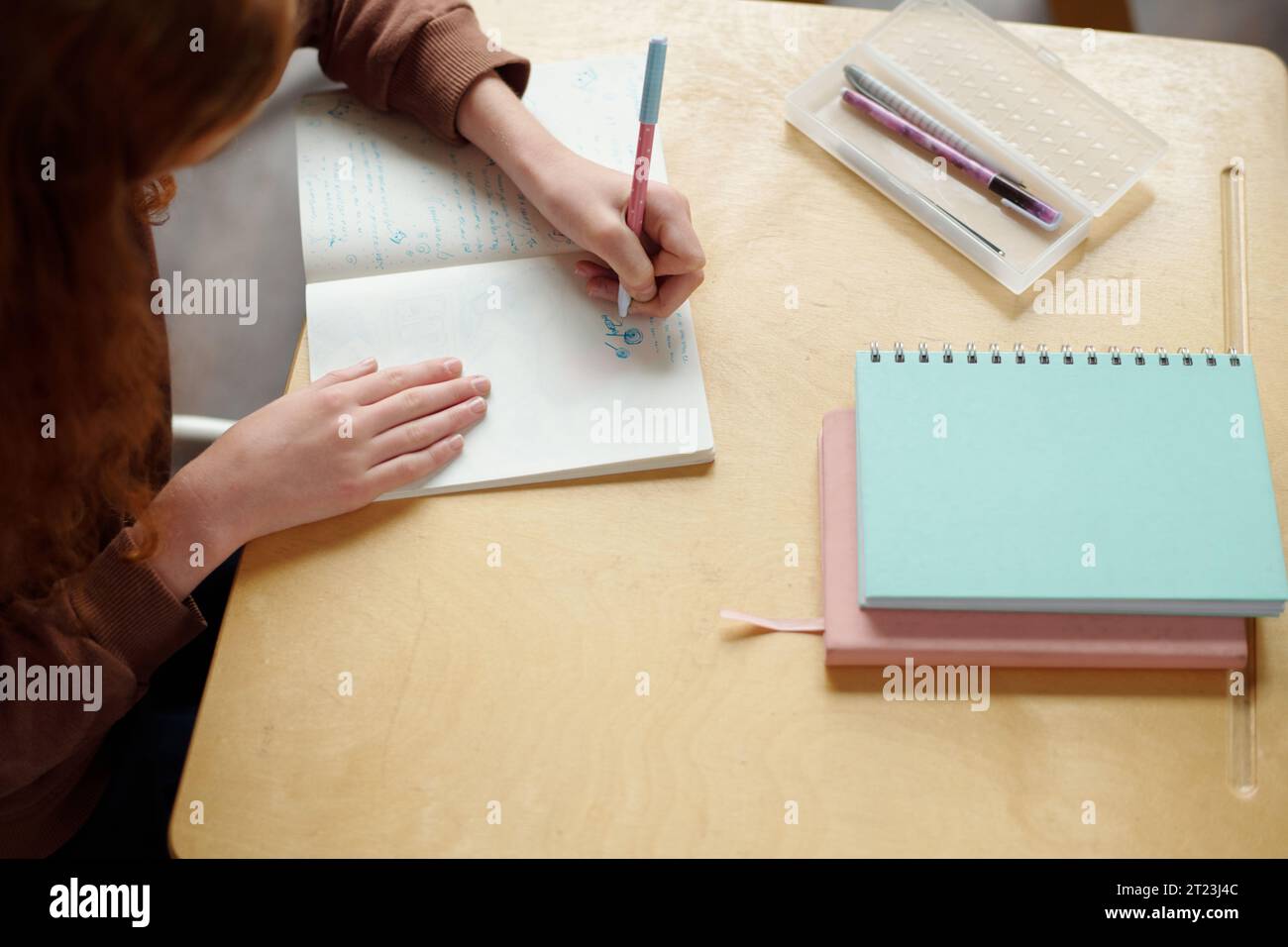 Über dem Winkel der Hände des Schülers der Sekundarstufe, der in einem Copybook mit Stift zeichnet, während er am Schreibtisch sitzt, während er am Unterricht des Englischgrammatikkurses sitzt Stockfoto