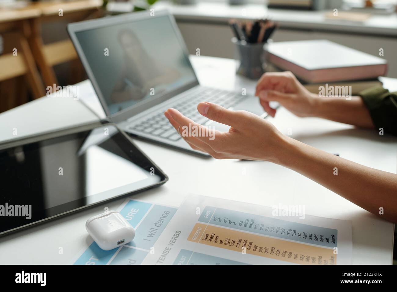 Konzentrieren Sie sich auf die Hand einer jungen Englischlehrerin, die der Schülerin während des Online-Unterrichts etwas auf dem Laptop-Bildschirm erklärt, während sie am Schreibtisch sitzt Stockfoto