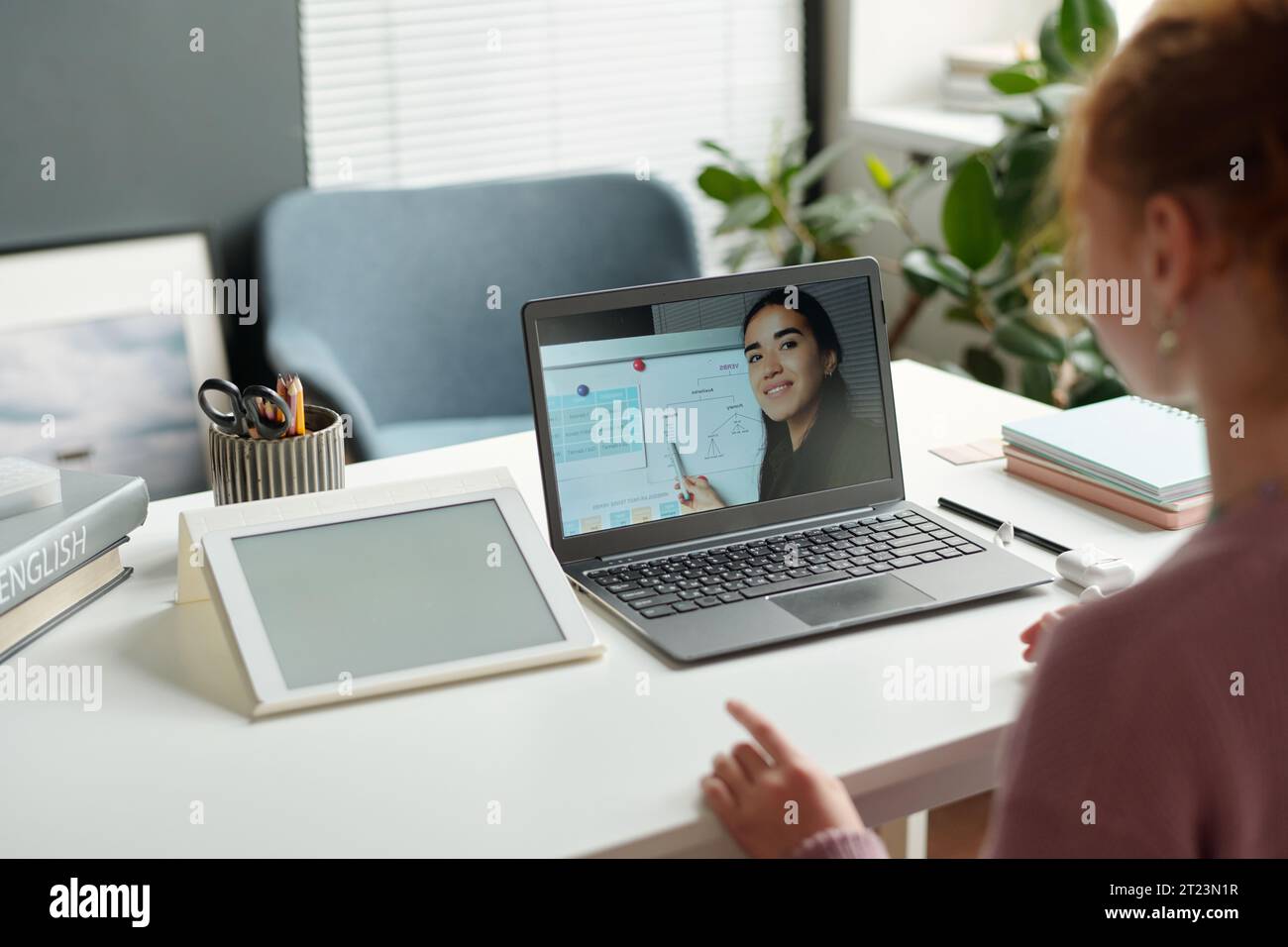 Konzentrieren Sie sich auf den Laptop-Bildschirm, während der Englischlehrer den Schülern der Sekundarstufe, die zu Hause am Schreibtisch sitzen, neue Grammatikregeln auf dem Whiteboard erklärt Stockfoto