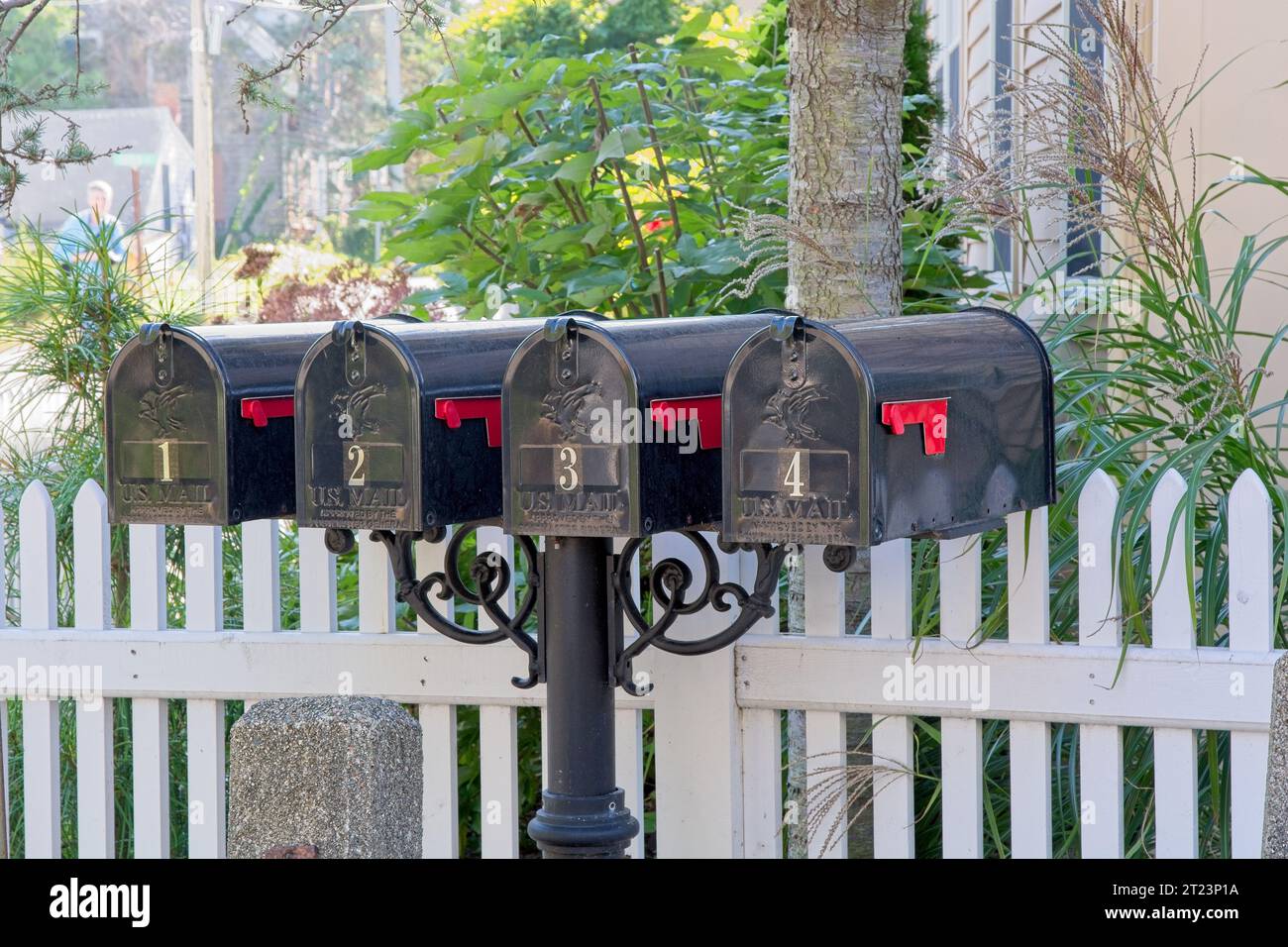 Set mit vier schwarzen Metall-US-Briefkästen auf Post vor weißem Pfostenzaun Stockfoto
