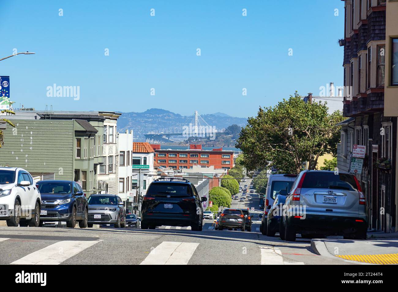 Ein Auto fährt eine Straße in San Francisco entlang, mit der Bay Bridge, weit entfernt. Stockfoto