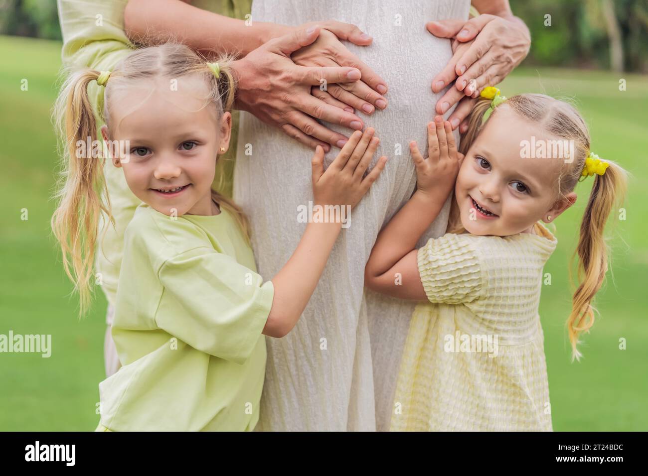 Die Liebe der Schwestern blüht, während sie den schwangeren Bauch ihrer Mutter zärtlich umarmen und ihre Vorfreude und Zuneigung für ihre bald ankommenden Geschwister teilen Stockfoto