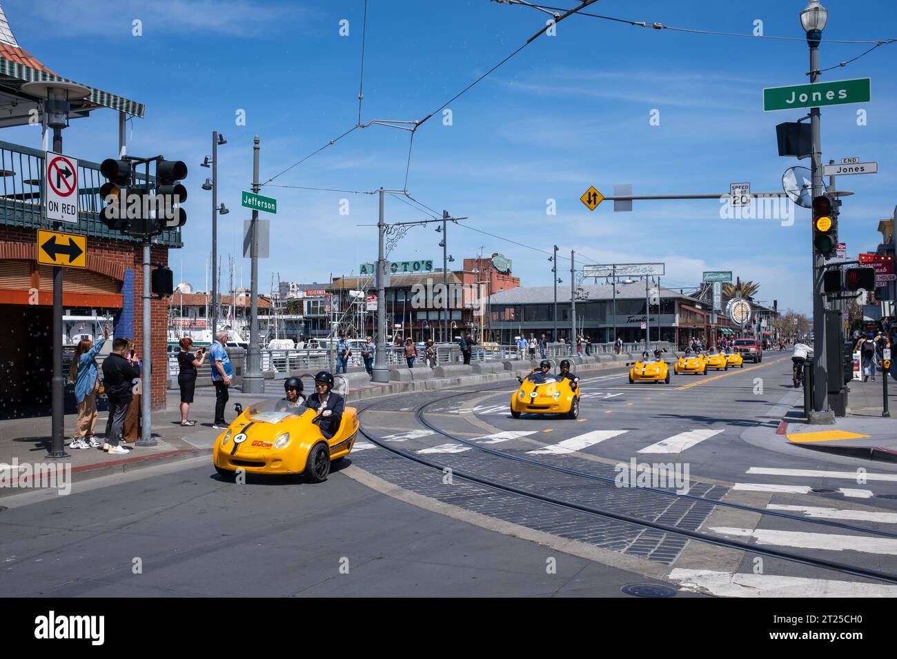 SAN FRANCISCO, USA - 21. April 2023: Touristen sitzen in zweisitzigen, gelben Miniwagen, die in der Nähe der Signalkreuzung anstehen und die Zuschauer anfeuern Stockfoto