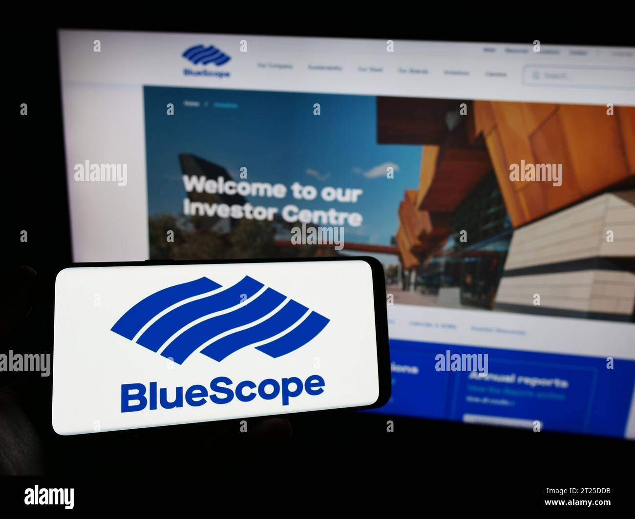Person, die ein Mobiltelefon mit dem Logo des australischen Unternehmens BlueScope Steel Limited vor der Webseite hält. Schwerpunkt auf dem Display des Telefons. Stockfoto