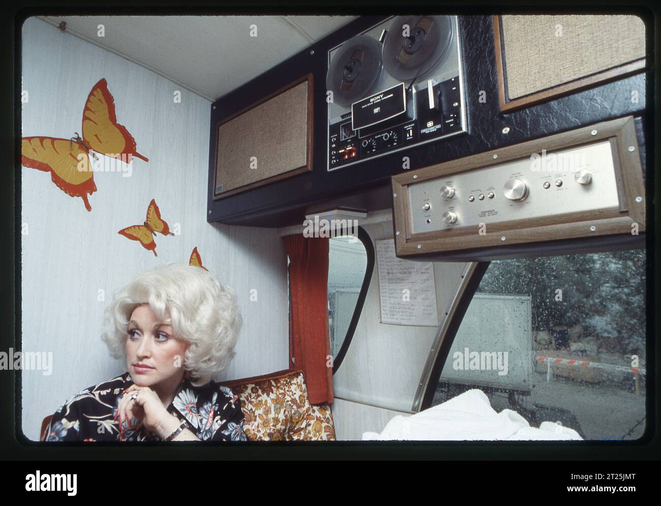 Dolly Parton wird in ihrem Tourbus interviewt und sitzt unter Stickern von Schmetterlingen und ihrer Stereoanlage. Stockfoto