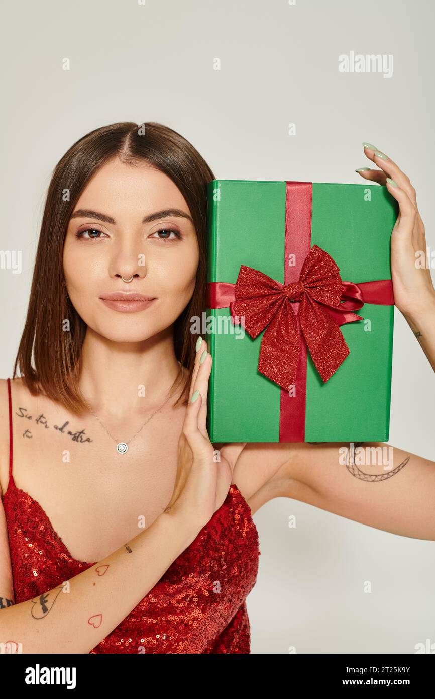 Attraktive Frau mit durchbohrter Nase und Tattoos, die Geschenk vor der Kamera zeigen, Weihnachtsgeschenke Konzept Stockfoto