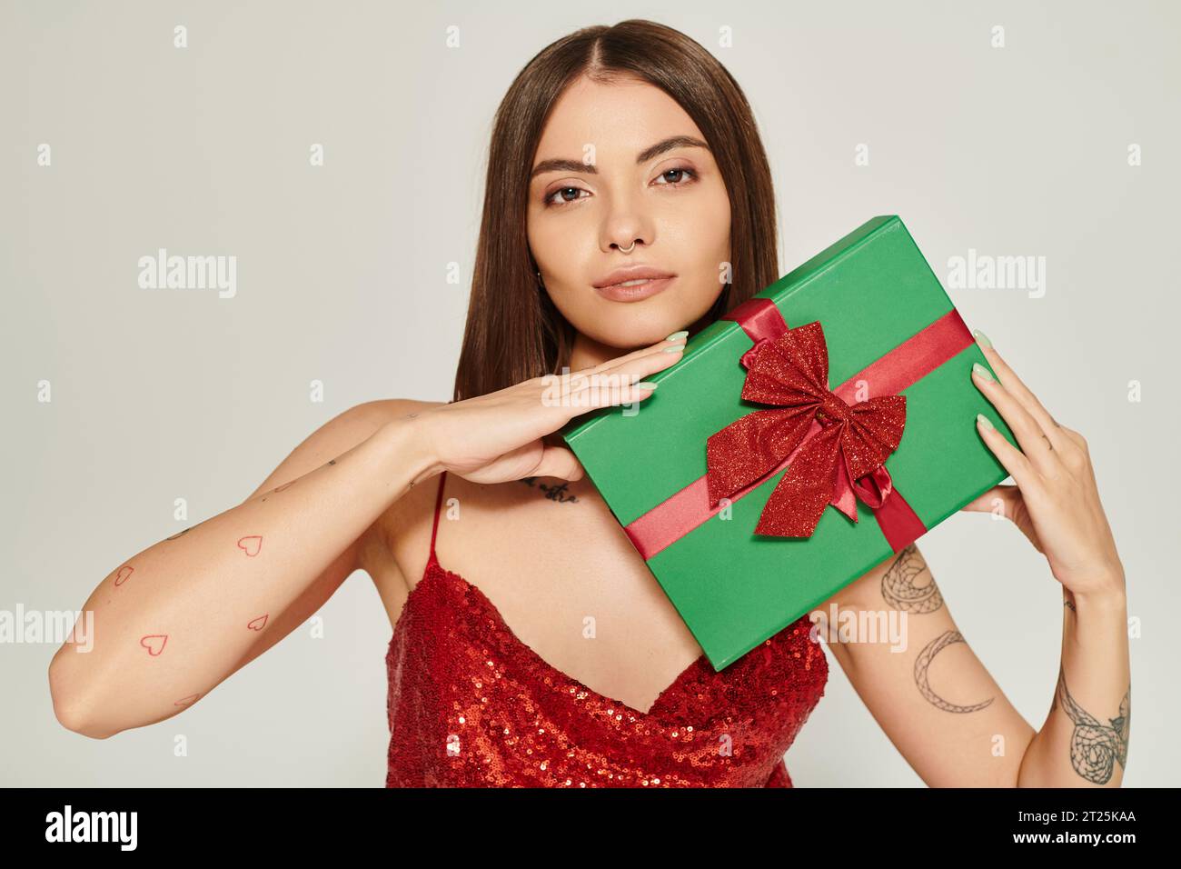 Schöne Frau mit Piercing und Tätowierungen mit Geschenk in den Händen, die in die Kamera schauen, Weihnachtsgeschenke Stockfoto