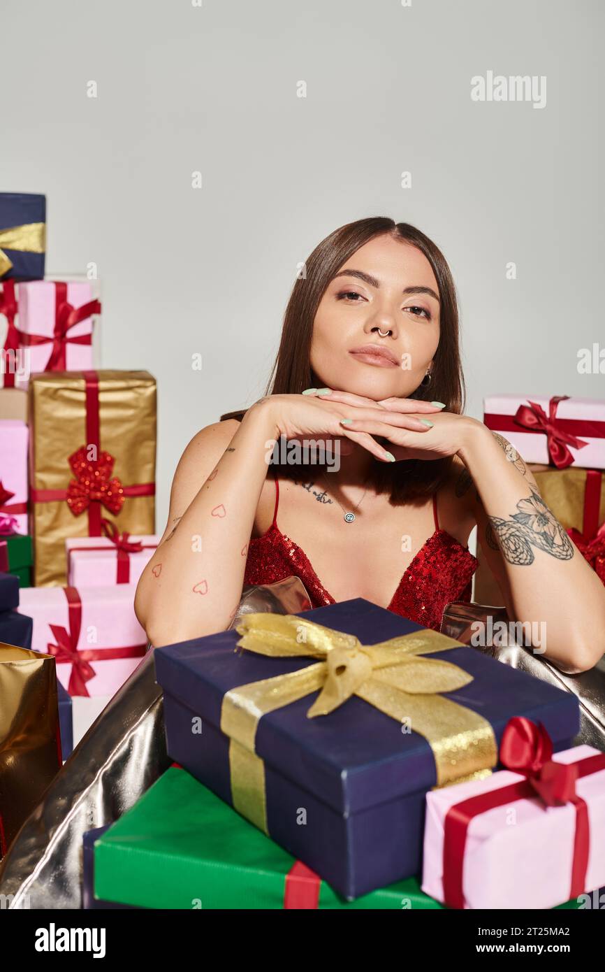 Schöne Frau mit Tattoos und durchbohrter Nase posiert mit Händen unter dem Kinn, Weihnachtsgeschenke Konzept Stockfoto