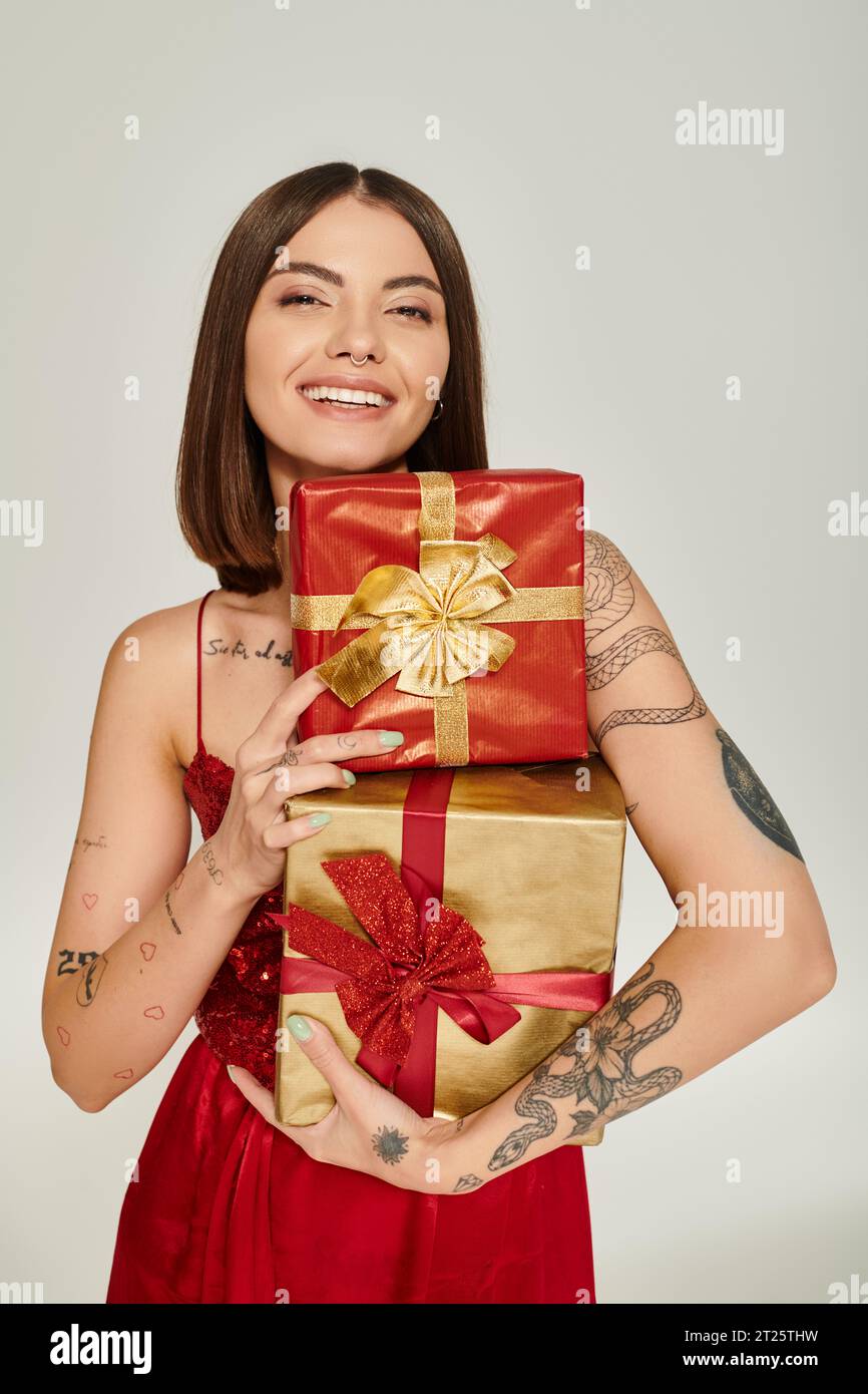 Attraktive, fröhliche Frau, die einen Haufen Geschenke hält und in die Kamera lächelt, Weihnachtsgeschenke Konzept Stockfoto