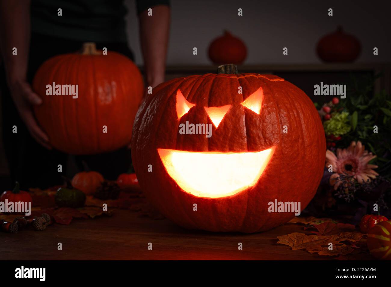 Augsburg, Bayern, Deutschland. Oktober 2023. Geschnitzter Halloween-Kürbis, dekoriert mit kleinen Hokkaido-Kürbissen in einem dunklen Zimmer, leuchtet aus dem bösen geschnitzten Mund. Halloween Dekoration *** Geschnitzer Halloween Kürbis dekoriert mit kleinen Hokkaido Kürbisen in einem dunklen Raum leuchtet aus dem fiesen geschnitzen Mund. Halloween Dekoration Credit: Imago/Alamy Live News Stockfoto