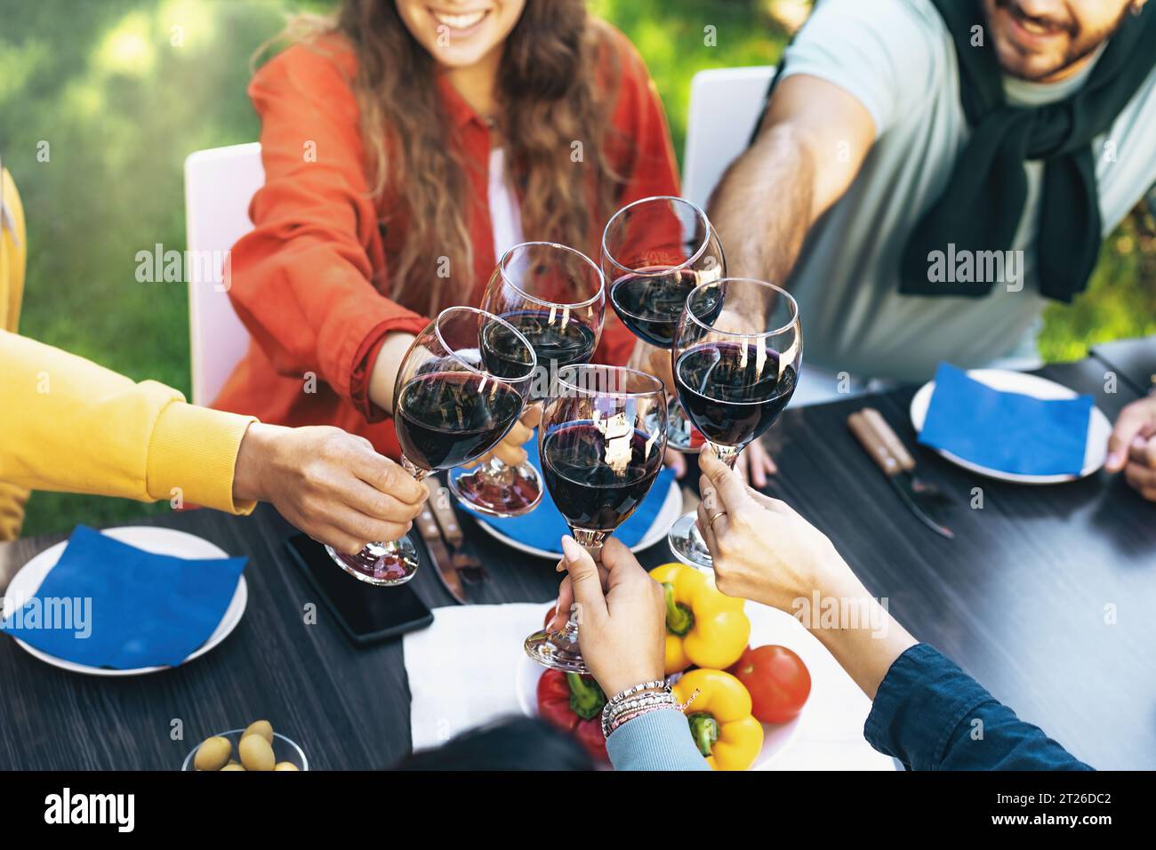 Ein Detail aus der Nähe von Weingläsern, die bei einem Toast auf einem Tisch im Innenhof anstoßen. Die unscharfen Gesichter der jungen Freunde deuten auf die Freude an Stockfoto