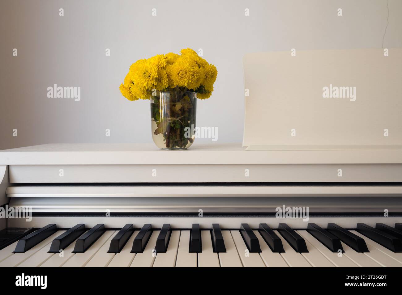 Weißes klassisches, modernes digitales Klavier mit offener Tastatur und Vase mit gelben Blumen. Einrichtung, Inneneinrichtung, Stil, Stillleben Stockfoto