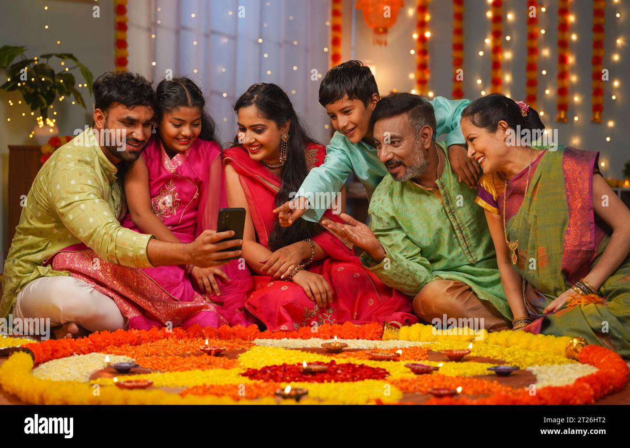 Gruppe von glücklichen indischen gemeinsamen Familie, die Handy während der Familie diwali Festival Feier vor der Blume Rangoli sieht - Konzept der emotionalen Stockfoto