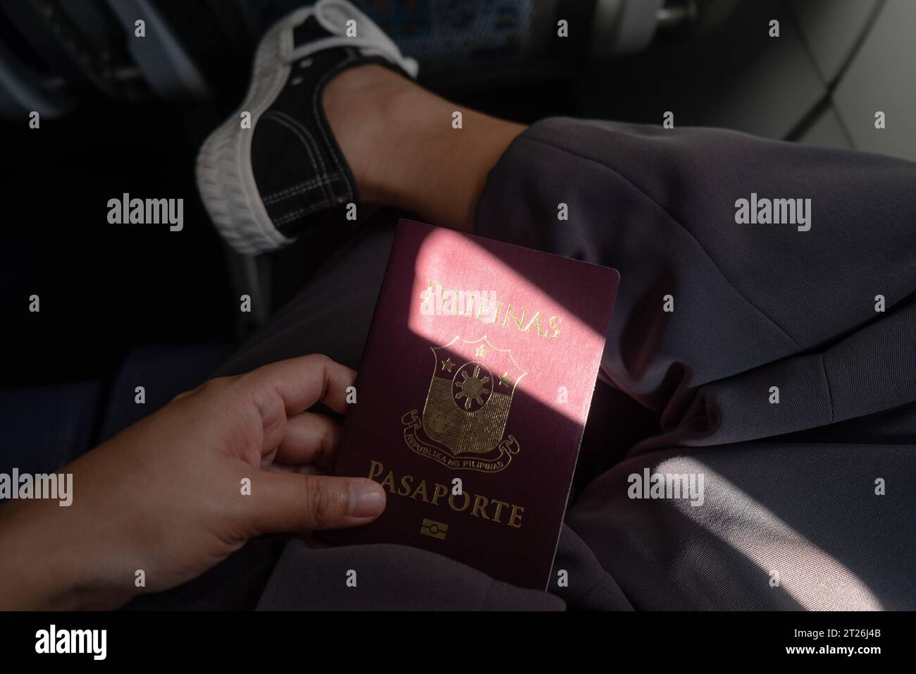 Weibliche Hand hält Philippine Passport auf der Runde mit überkreuztem Bein. Passagier im Flugzeug. Auslandsaufenthalt von philippinischen Arbeitnehmern. Kreativer Reisehintergrund. Stockfoto