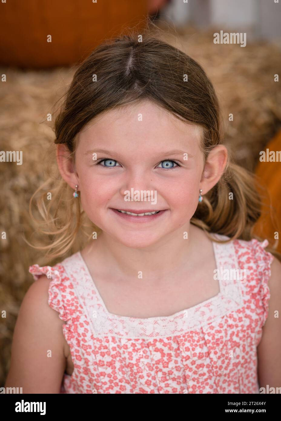 Nahaufnahme Porträt eines 5-jährigen Mädchens mit Ohrringen, das auf Heu an einem Kürbisfeld in San Pedro sitzt. Stockfoto