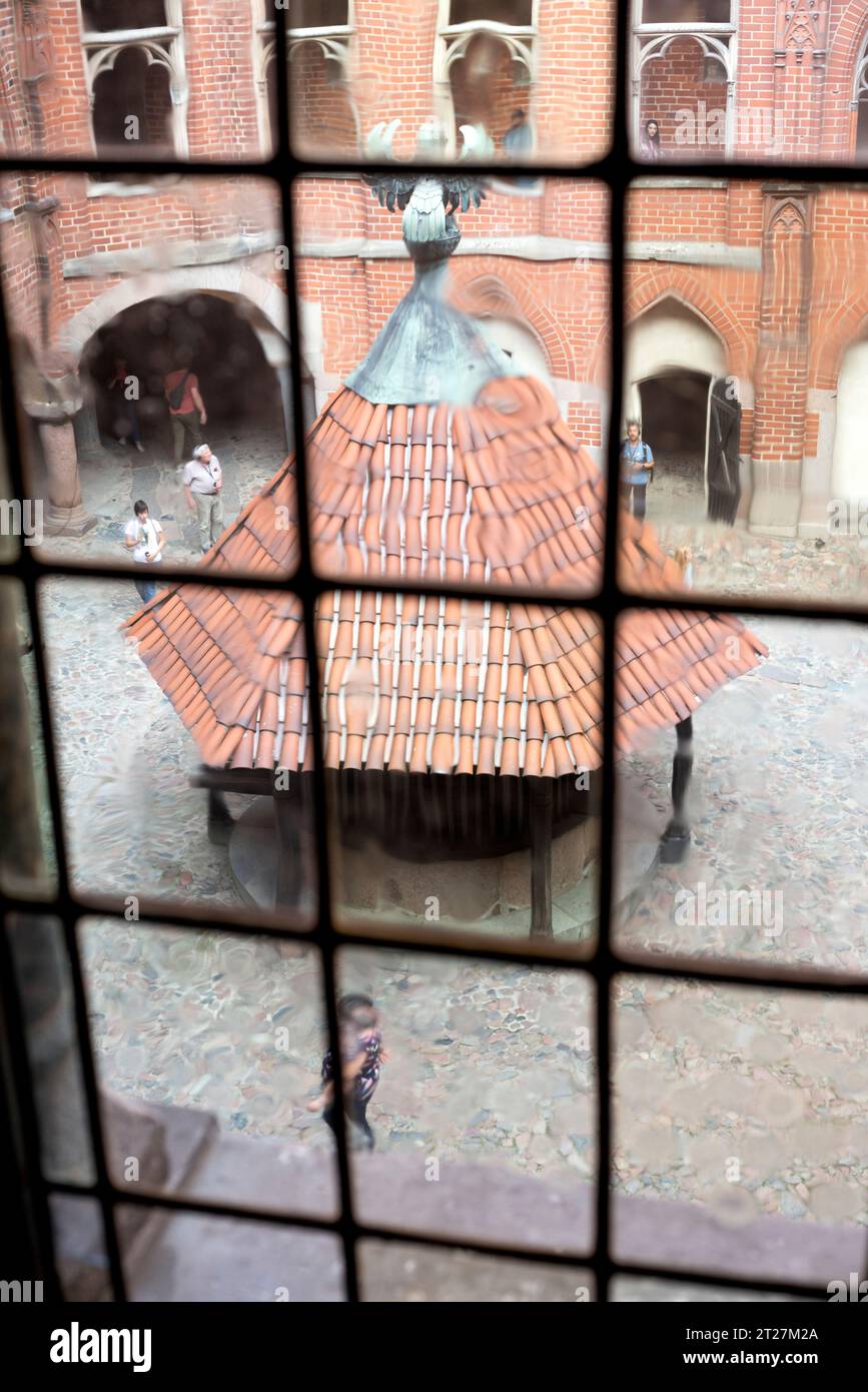 Blick durch ein Fenster auf den Brunnen im Innenhof des Hochschlosses in der Burg Malbork, Malbork, Polen, Europa, EU Stockfoto