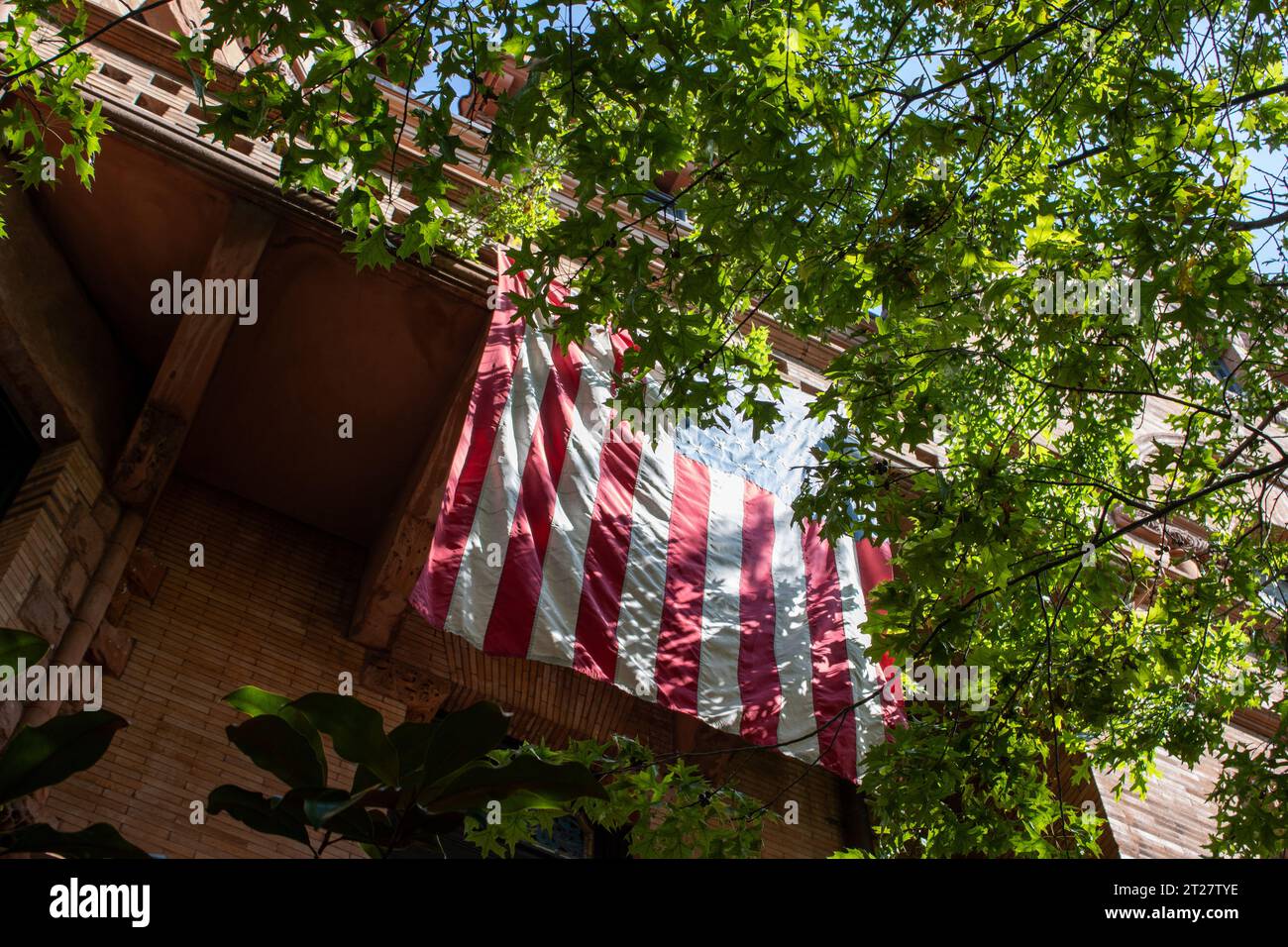 amerikanische Flagge hängt bei Tageslicht über dem Balkon hinter einigen Bäumen Stockfoto