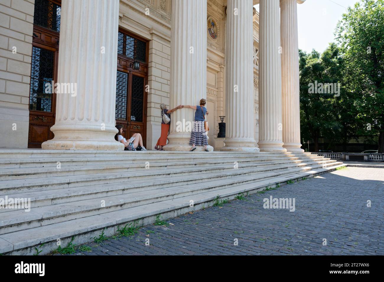 Menschen umarmen eine Säule im rumänischen athenäum, während ein teenager sitzt und liest Stockfoto