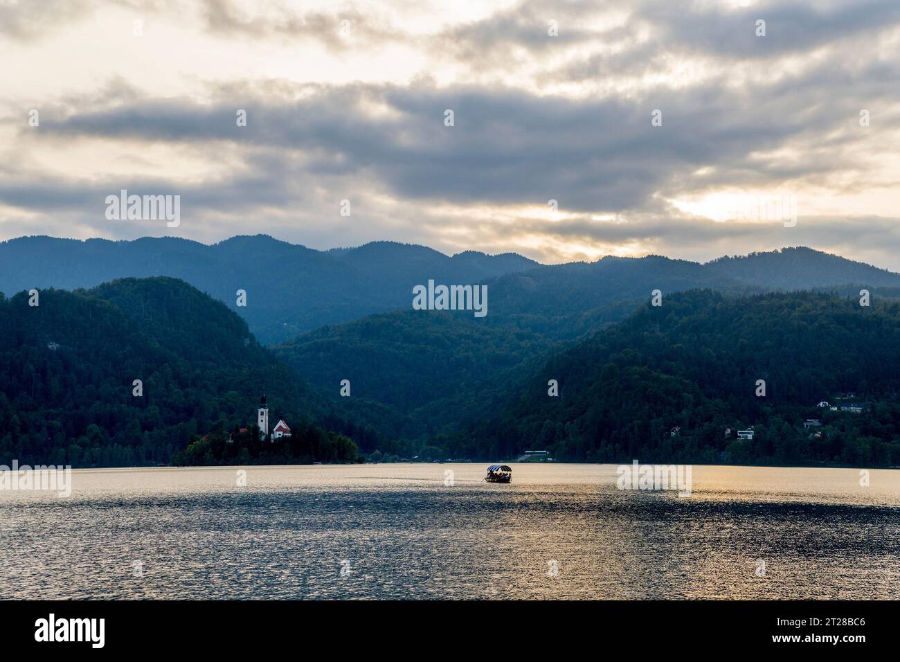 Touristen auf einem Pletna-Boot, traditionelle Boote, die von den Einheimischen von Bled handgefertigt werden, besuchen Bled Island (dunkler, bewölkter Himmel) mitten im Bleder See, Slov Stockfoto