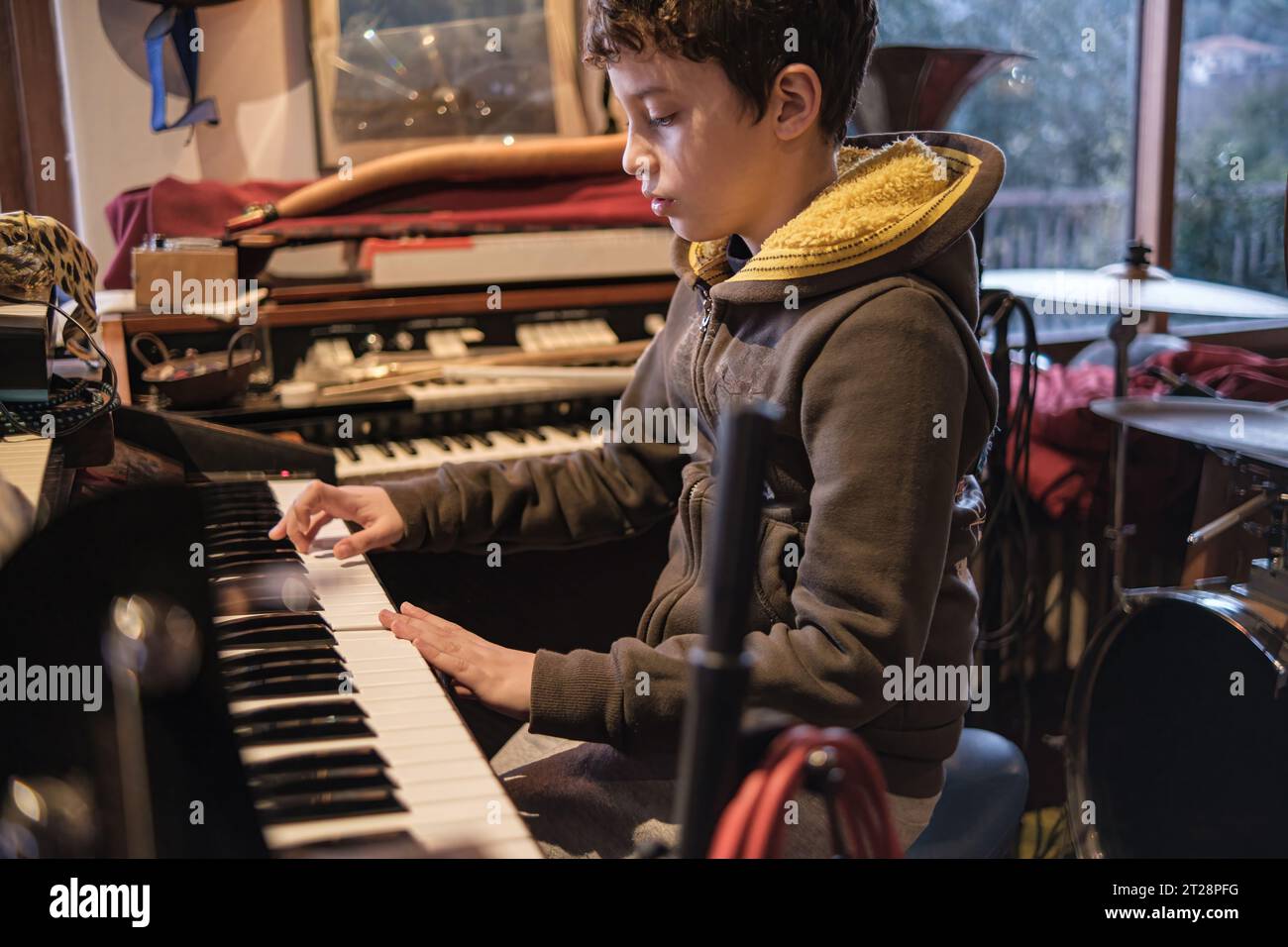 Ein 10-jähriges Kind zeigt sein Talent und spielt leidenschaftlich die Orgel in einem Proberaum, eingetaucht in die Welt der Musik. Stockfoto