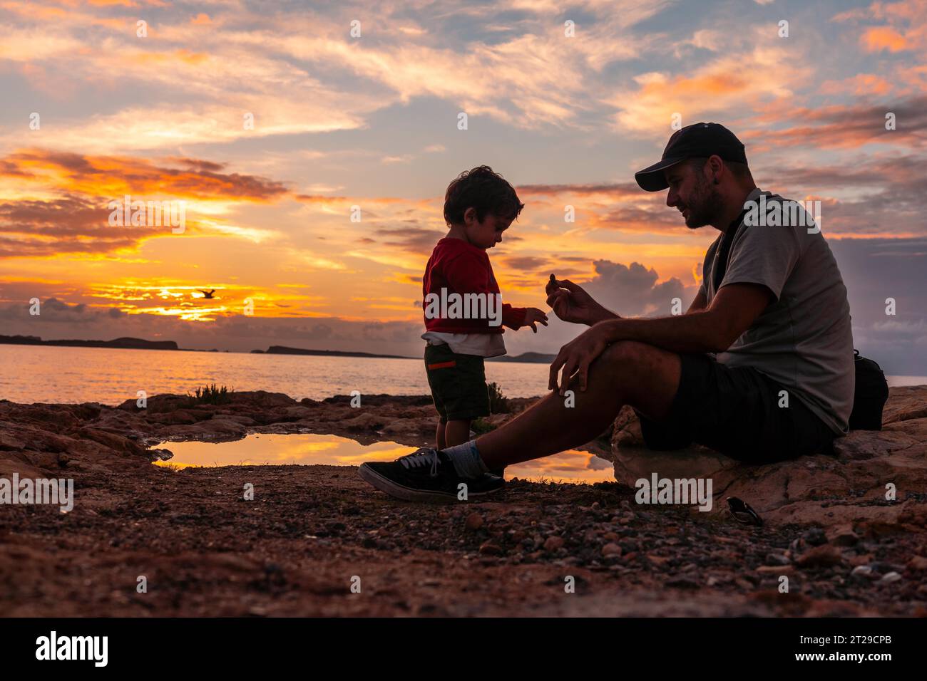 Sonnenuntergang auf Ibiza im Urlaub, junger Vater mit seinem Sohn genießt am Meer in San Antonio Abad Stockfoto