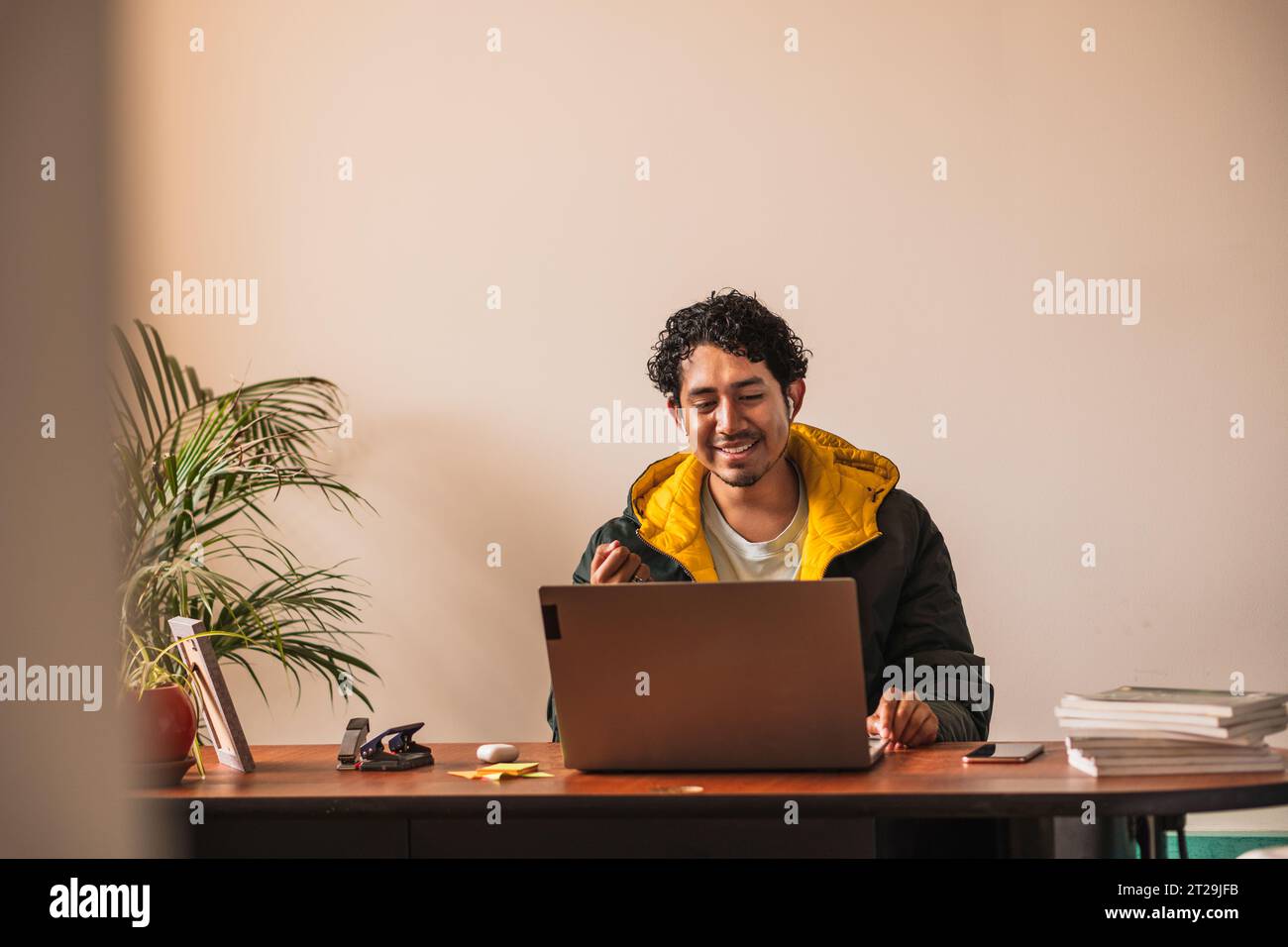 Positiver männlicher Remotearbeiter, der Netbook für Online-Projekte verwendet, während er in unscharfem Hintergrund am Tisch arbeitet Stockfoto