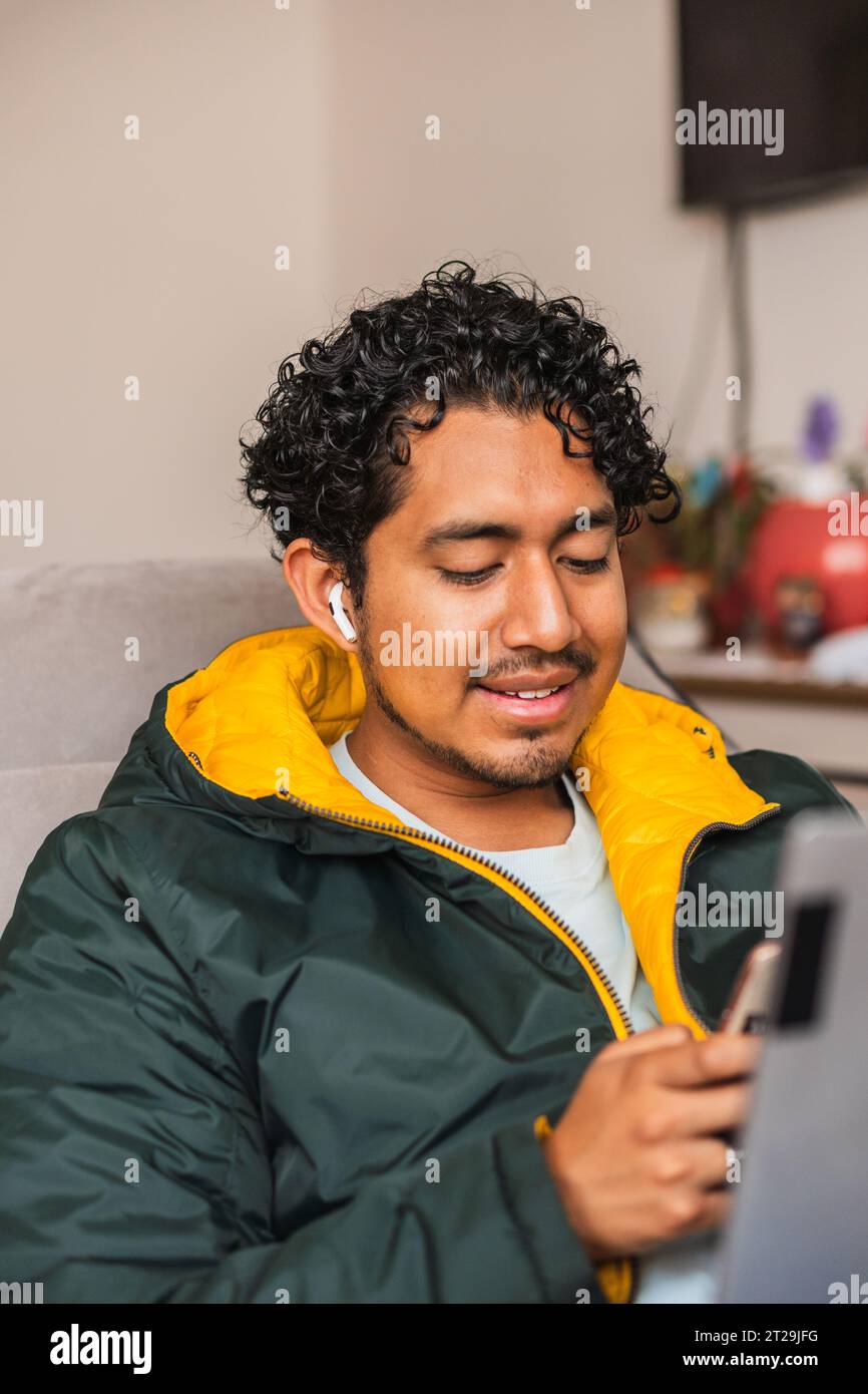 Positiver männlicher Remotearbeiter, der Netbook und Telefon für Online-Projekte verwendet, während er in unscharfem Hintergrund am Tisch arbeitet Stockfoto