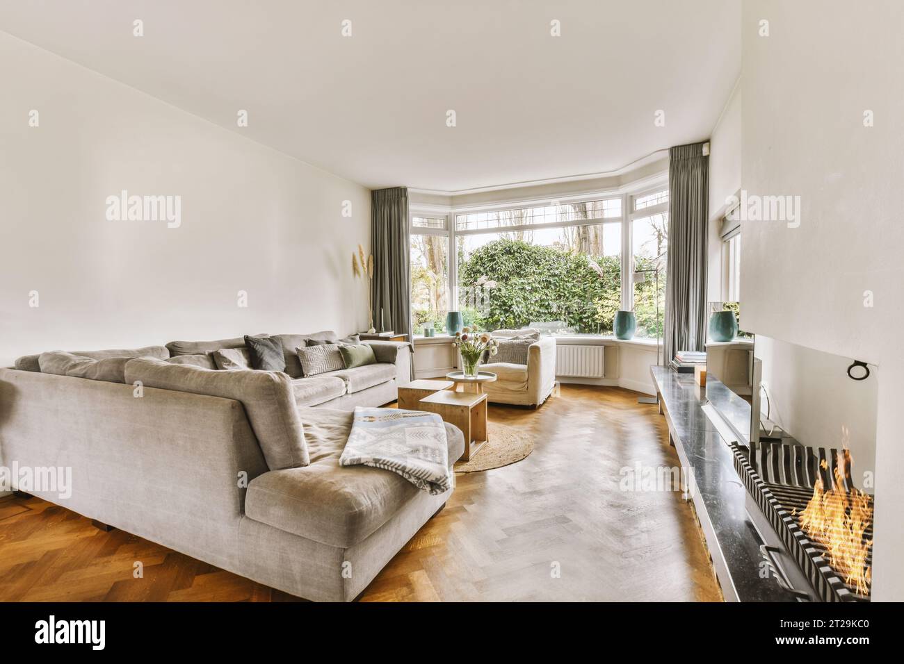 Das Innere des geräumigen Wohnzimmers mit großer Couch vor dem Fernseher und Kamin zu Hause vor einem großen Fenster Stockfoto