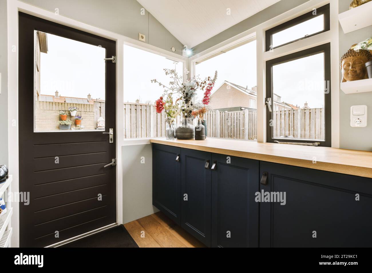 Blumenvasen auf Holzküche und schwarze Schränke mit hellen Fenstern im modernen Haus Stockfoto
