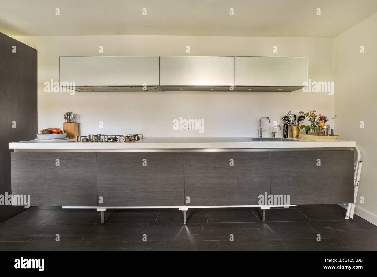 Moderne Küche mit sauberer langer weißer Arbeitsfläche und Stahlwaschbecken mit grauen Schränken in einem modernen Apartment Stockfoto