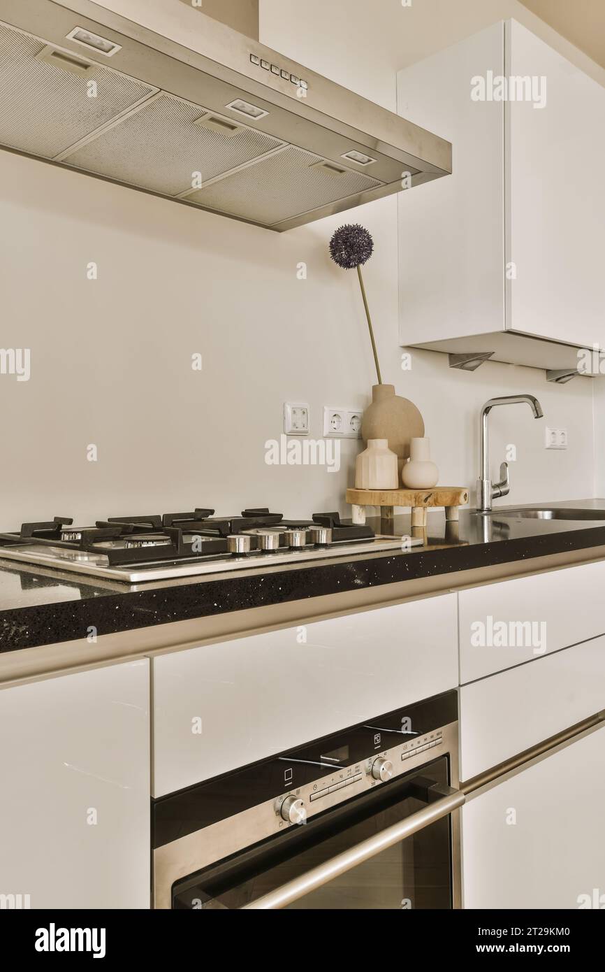 Chrom-Sichtbarkeit über Herd auf schwarzer Arbeitsplatte und weiße Schränke in moderner Küche in einem modernen Zuhause Stockfoto