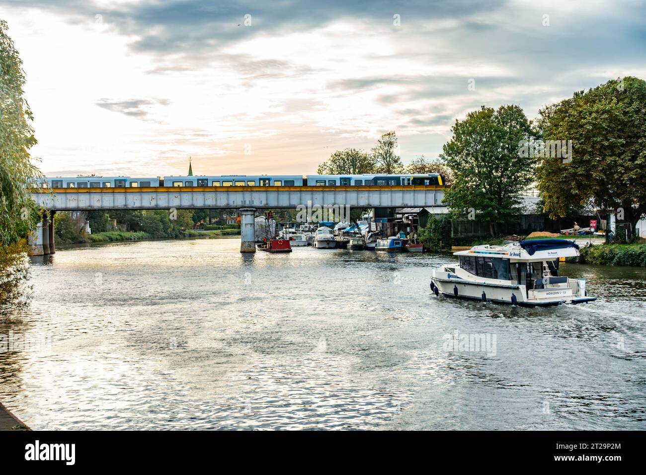 Ein Blick auf die Themse bei Staines-upon-Thames in Surrey, Großbritannien, in Richtung einer Eisenbahnbrücke, die den Fluss überspannt. Stockfoto